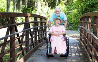 Senior man pushes his disabled wife through the park in a wheelchair.
